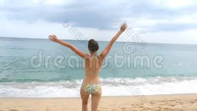 跟随年轻快乐的女人在海滩上向海洋跑去，举起双手。 美丽的女孩在沙滩上慢跑